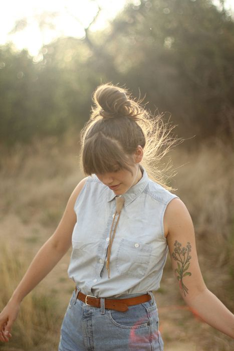 a woman with her hair in a bun wearing jeans and a shirt is walking through the grass