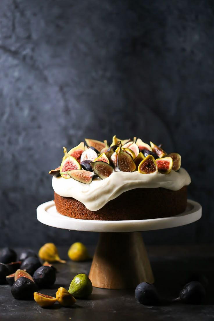 a cake with white frosting and figs around it on a plate next to some olives