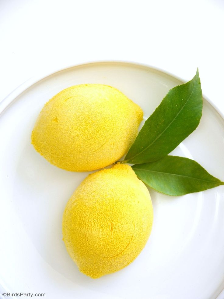 two lemons with green leaves on a white plate