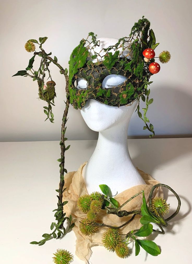 a white mannequin head with green plants and berries on it's face