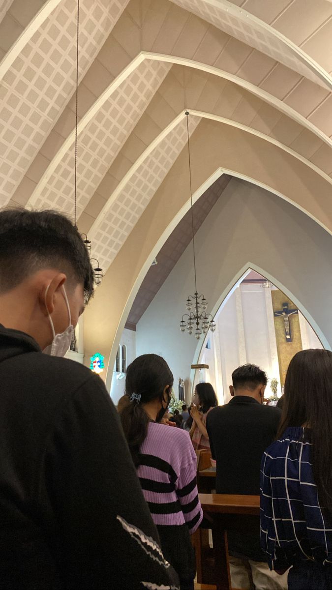 a group of people standing in front of a church pew with the cross hanging from it's ceiling