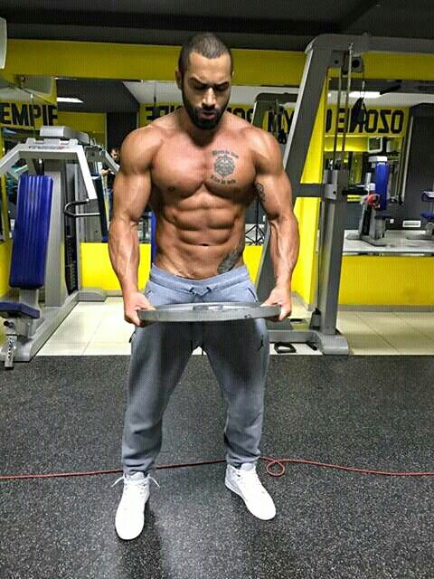 a shirtless man holding a weight plate in a gym