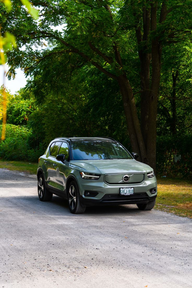 a green car parked on the side of a road next to some tall trees and grass