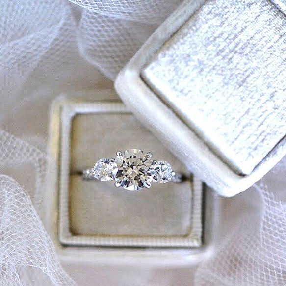 an engagement ring sitting on top of a white cloth covered box next to a veil