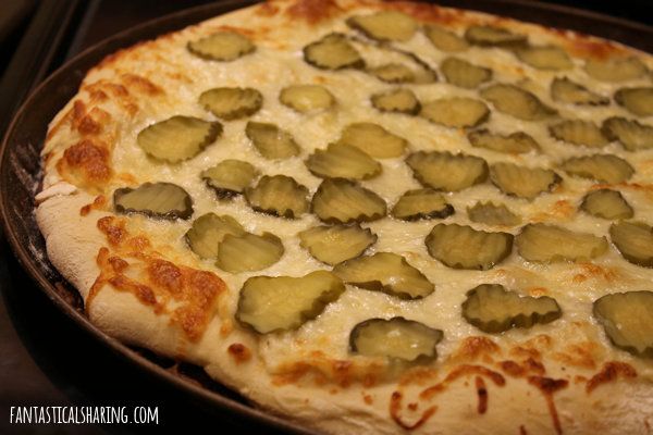 a pizza with cheese and pickles on it sitting in a baking pan, ready to be baked