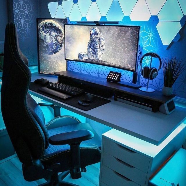 a computer desk with two monitors and headphones on it, lit up by blue lights