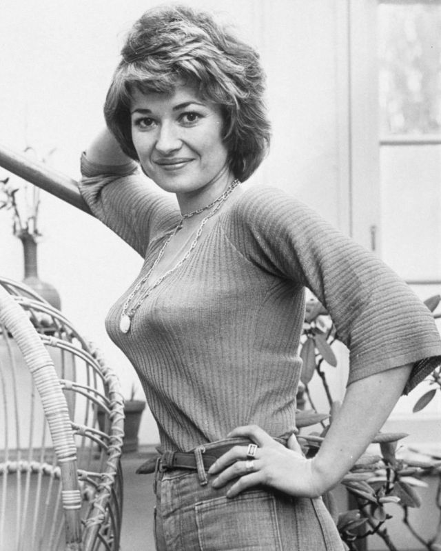 black and white photo of woman holding baseball bat in her right hand while standing next to wicker chair