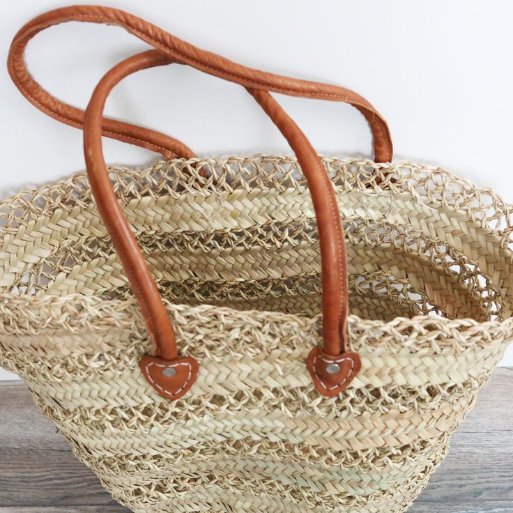 This sturdy Large Lace Straw Market Basket is handwoven from natural palm leaves for a unique and beautiful boho chic look. Its classic lace style and ancestral craftsmanship make it perfect for a farmers market haul or a day at the beach. Each basket is crafted with skill by female artisans. dimensions: height: 14", width: 19", base: 6" x 11" // 35cm H, 48cm W, 15*28cm baseleather strap: 10" high // 25cm style:two different styles of handles: braided or plain leather*because each basket is hand Bohemian Straw Bag With Woven Leather In Natural Color, Bohemian Beige Beach Bag With Woven Leather, Braided Jute Beach Bag In Natural Color, Natural Jute Braided Beach Bag, Bohemian Beige Leather Woven Beach Bag, Natural Braided Jute Beach Bag, Traditional Natural Straw Bag With Open Weave, Bohemian Brown Straw Bag With Woven Leather, Brown Bohemian Straw Bag With Open Weave