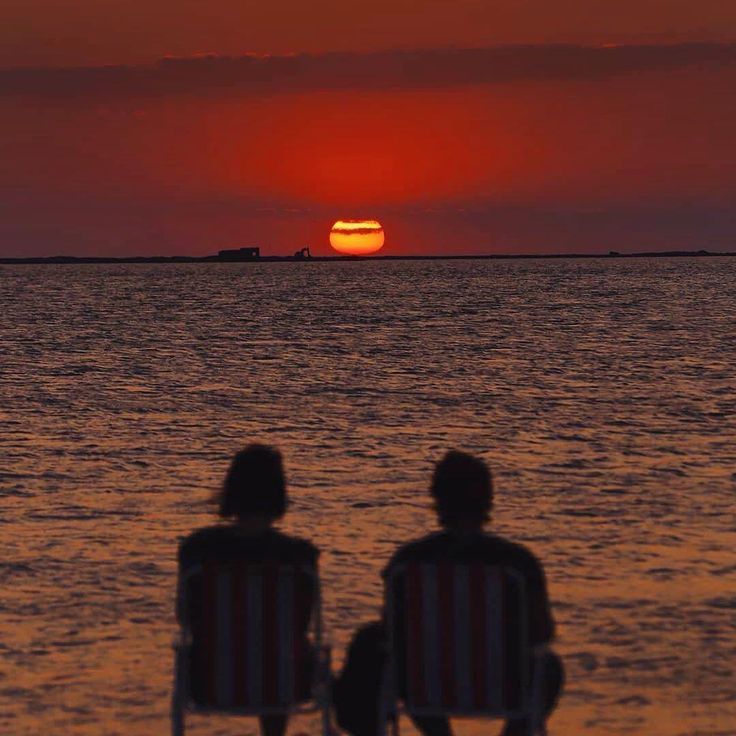 two people sitting in chairs watching the sun set