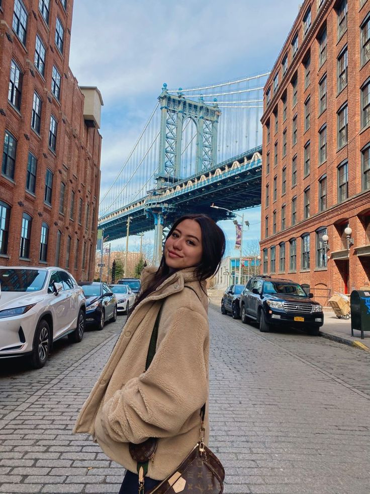 a woman is standing on the street in front of some buildings with a bridge behind her