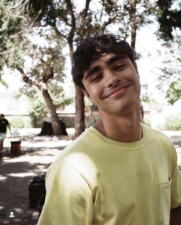 a young man standing in front of trees smiling at the camera with his eyes closed