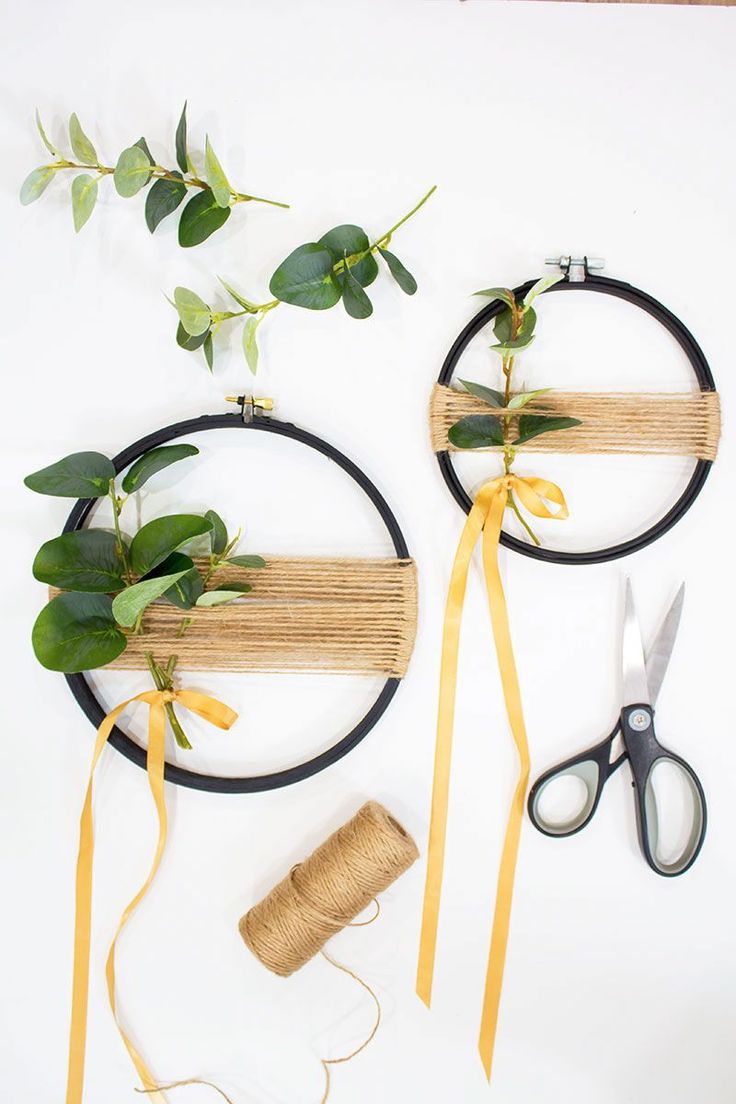 two round wooden frames with plants and scissors next to each other on a white surface