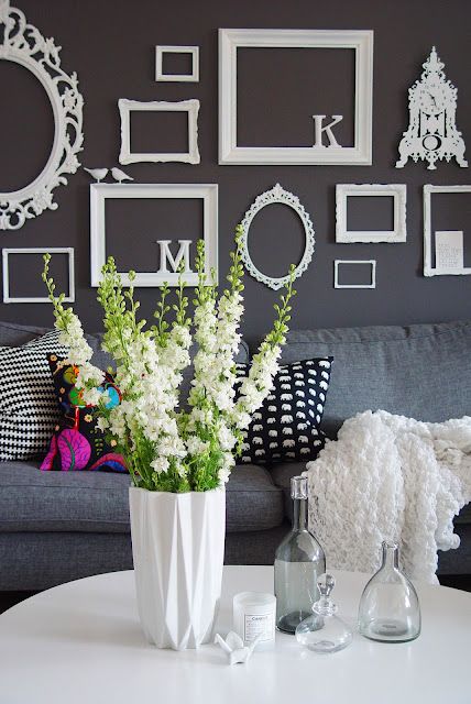 a vase with flowers on a table in front of a gray couch and black and white wall