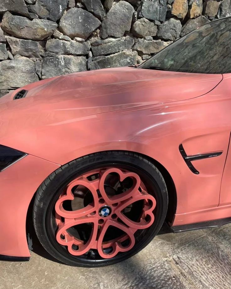 a pink sports car parked in front of a stone wall with red spokes on it