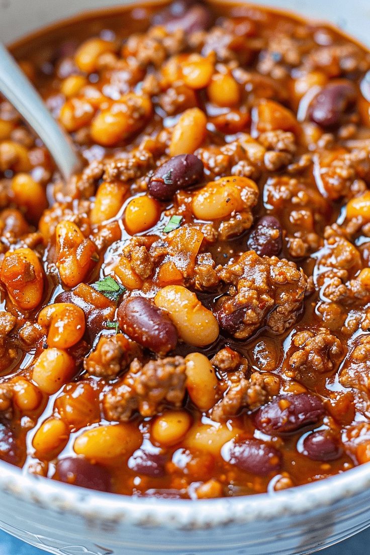 a bowl filled with chili and beans on top of a blue table cloth next to a spoon