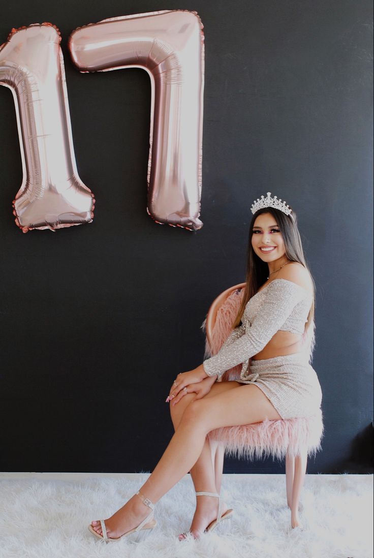 a woman sitting on top of a chair next to a giant pink letter m balloon