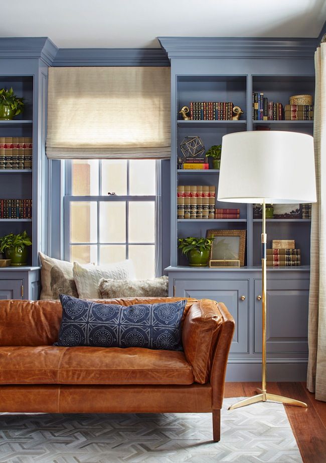 a brown leather couch sitting in front of a book shelf filled with books and pillows