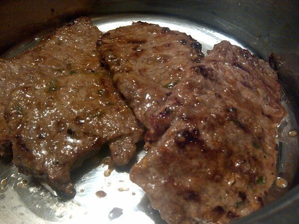 two steaks cooking in a pan on the stove