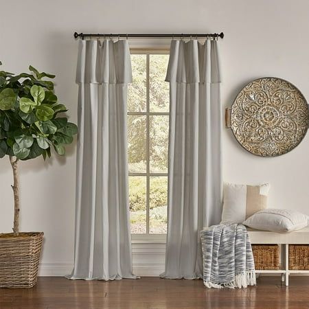 a living room with white walls and wood flooring, two windows covered in curtains