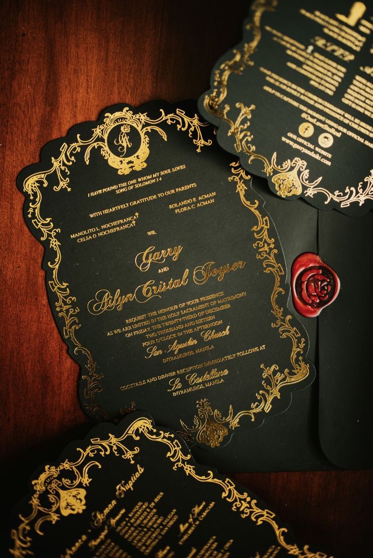 two black and gold wedding cards with red wax stamp on them, sitting next to each other