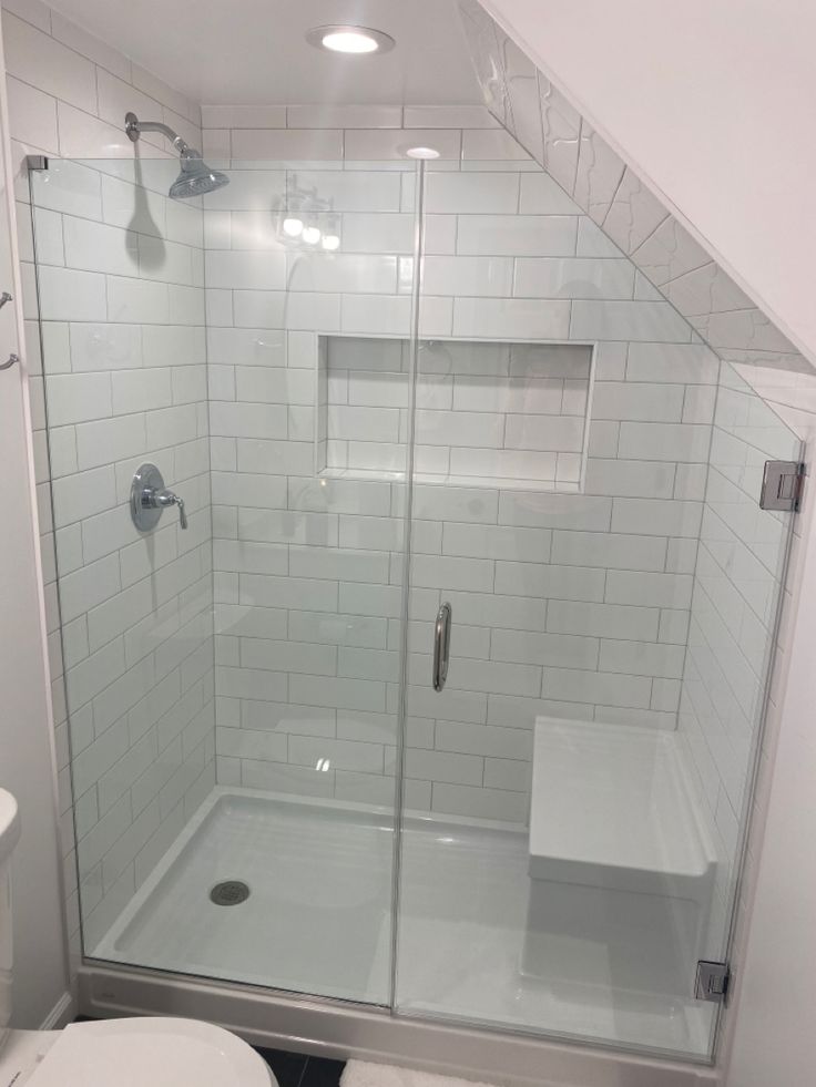 a white toilet sitting next to a shower in a bathroom under a slanted ceiling