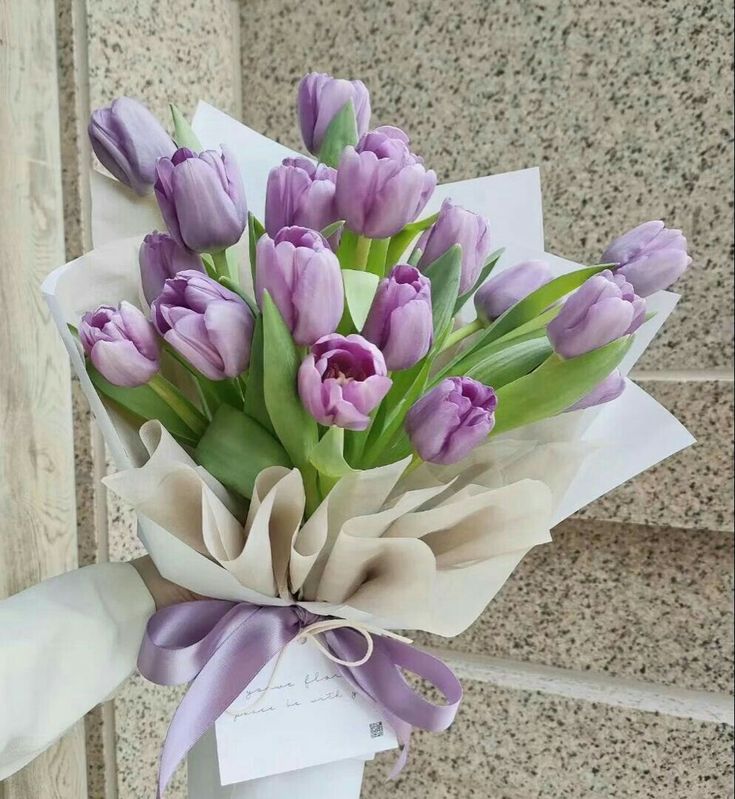 a bouquet of purple tulips wrapped in white paper