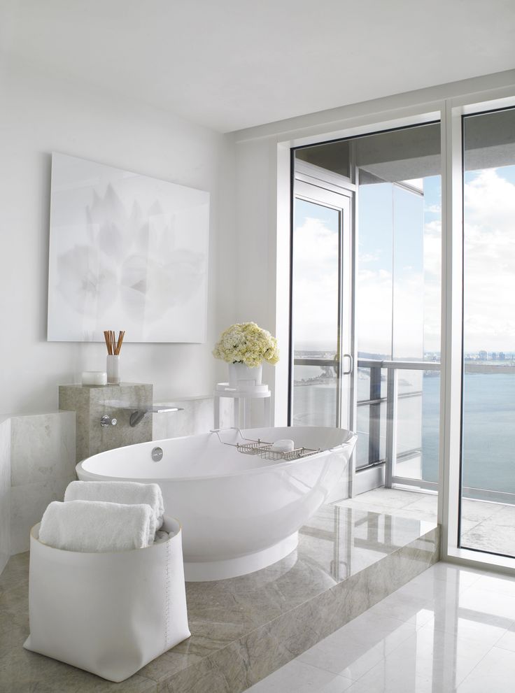 a large white bathtub sitting next to a window in a bathroom near the ocean