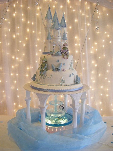 a white cake with blue frosting and fairy lights on the wall in front of it