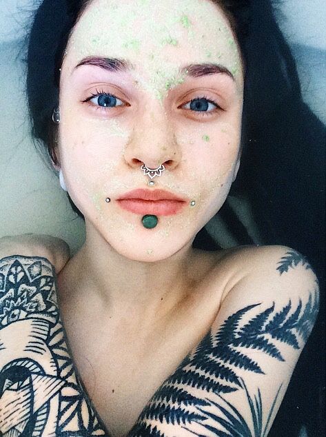 a woman with tattoos and piercings on her face is posing for the camera while wearing a green nose ring