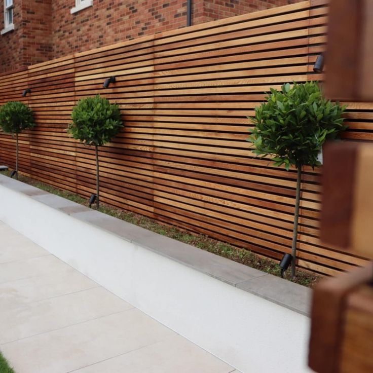 a wooden fence next to a building with trees on the side and grass in front