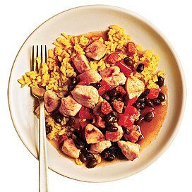 a white plate topped with rice, beans and meat next to a knife and fork