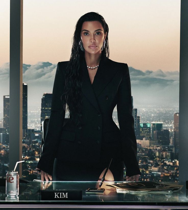 a woman standing in front of a window next to a desk with a laptop on it