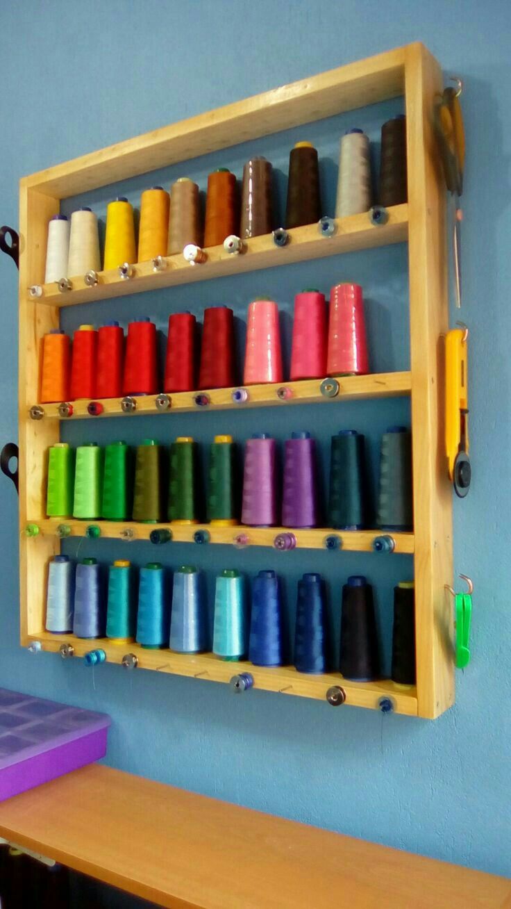 a wooden shelf filled with lots of spools of thread on top of a blue wall