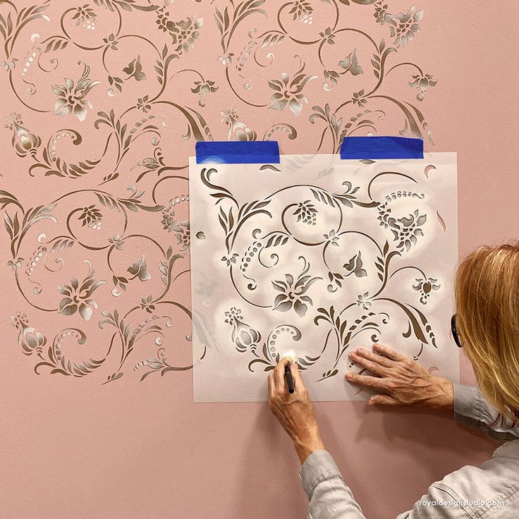 a woman is using stencil to decorate a wall with flowers and vines on it