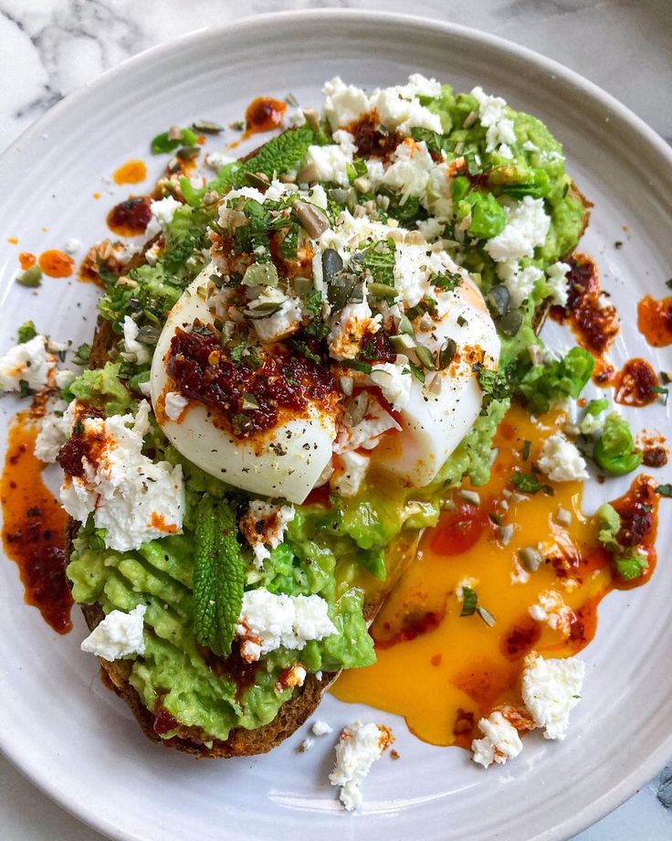 a white plate topped with an egg and lettuce covered in feta cheese