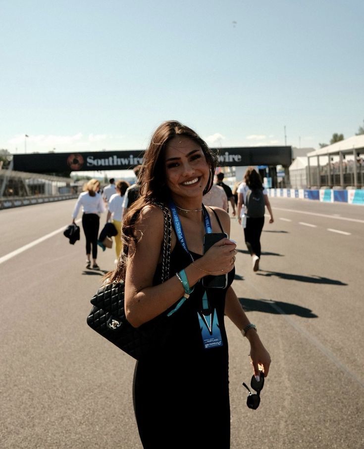 a woman standing on the side of a race track holding a cell phone in her hand