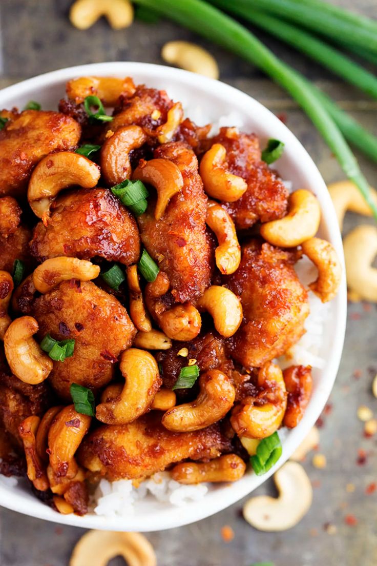 a white bowl filled with cashews and chicken on top of rice next to green onions