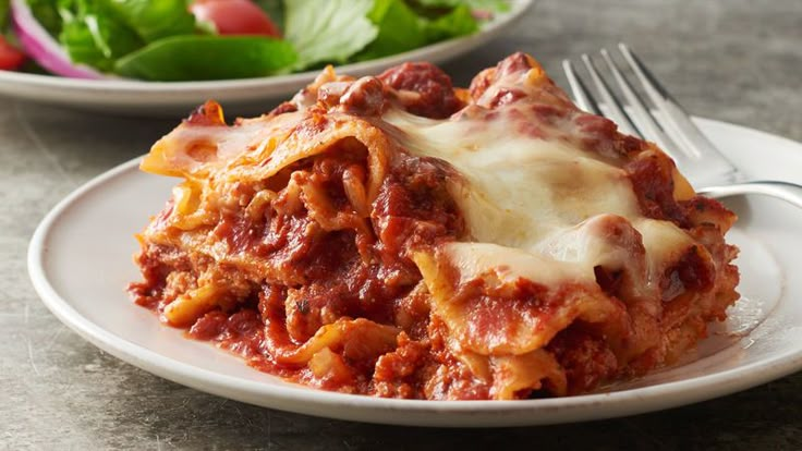 a white plate topped with lasagna next to a bowl of salad