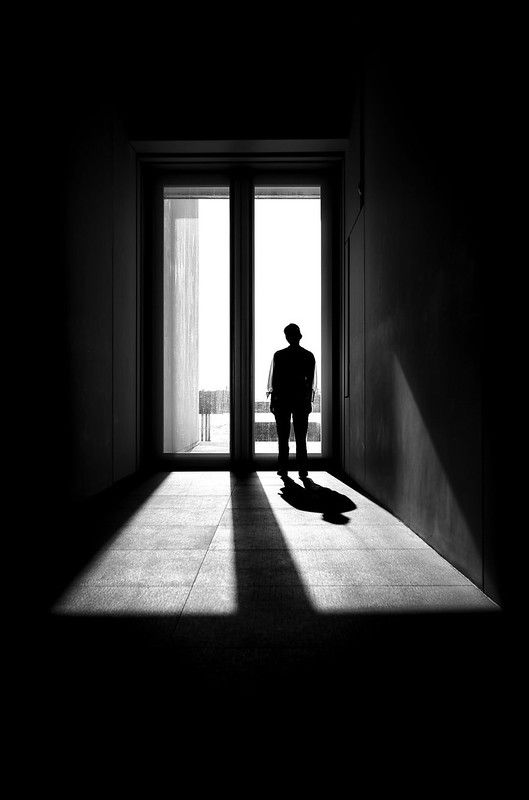 a man standing in front of an open door with his shadow on the floor and light coming through