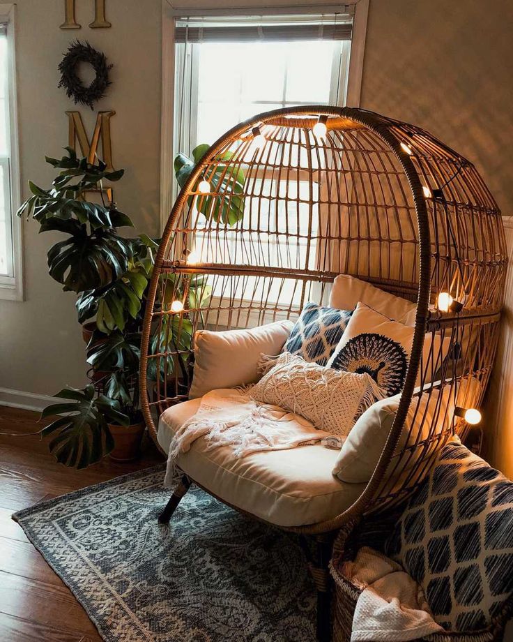 a rattan swing chair with lights on it in front of a window and potted plant