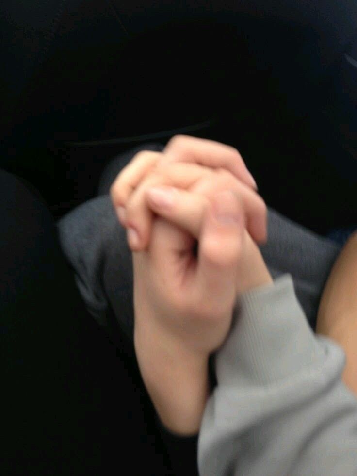 a person holding the hand of another person in a car with their hands clasped together