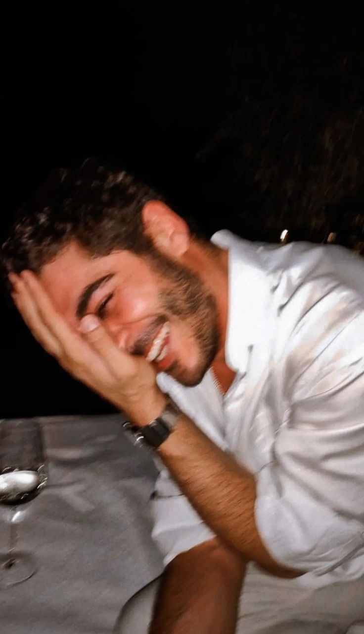 a man sitting at a table laughing and holding his hands to his face with one hand