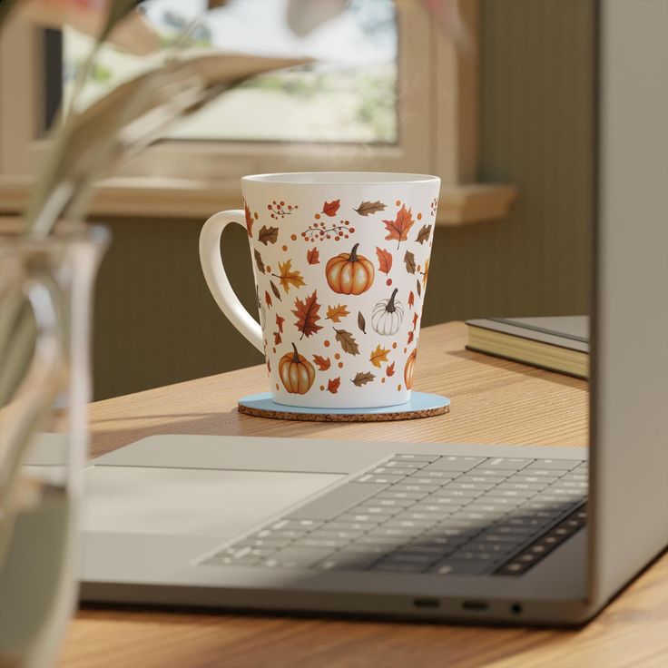 a coffee cup sitting on top of a wooden table next to a laptop computer and potted plant