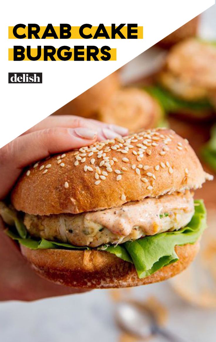 a hand holding a sandwich with lettuce and chicken on it, in front of other burgers