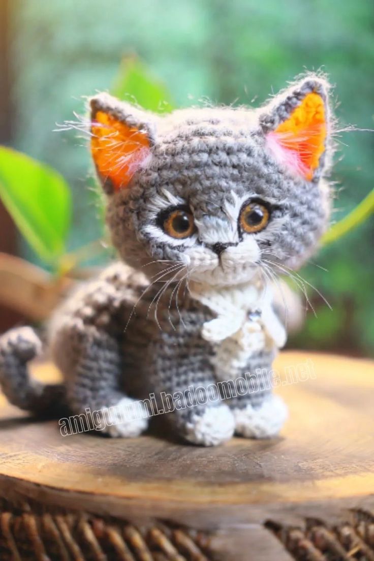 a small crocheted kitten sitting on top of a wooden table next to a plant