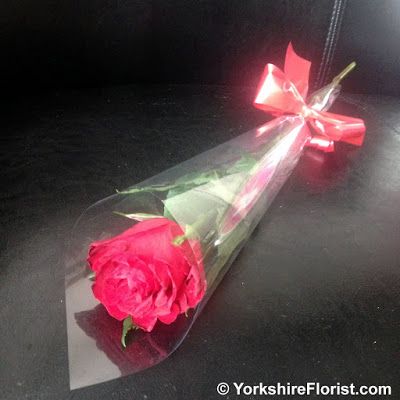 a single red rose wrapped in clear cellophane and tied with a ribbon on a black surface