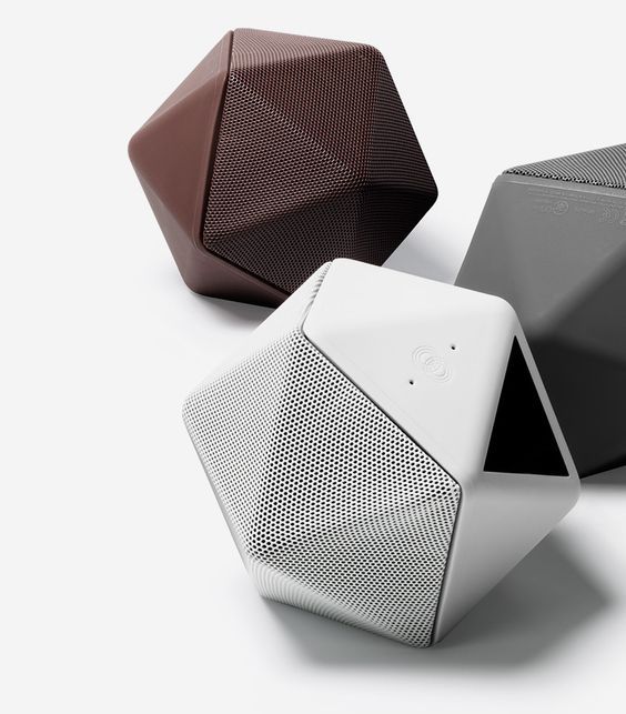 three different colored speakers sitting next to each other on a white surface with one speaker in the middle