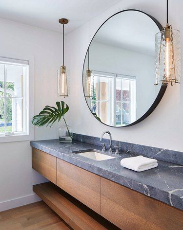 a bathroom with two sinks and a large round mirror above the sink, along with a plant