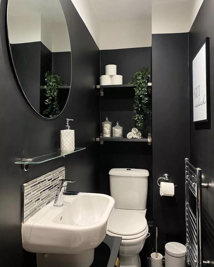 a white toilet sitting next to a bathroom sink under a round mirror in a black and white bathroom