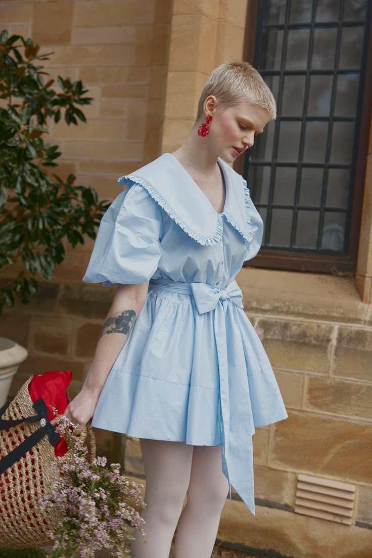 Elevate your Spring wardrobe with the Hazel Mini Dress, a radiant creation cut from blue cotton. It boasts a generous Peter Pan collar with a deep V neck, ensuring a flattering and elegant neckline. The sleeves are adorned with meticulously crafted tucks and gathers, lending an artful and exaggerated silhouette.  The piece is beautifully finished with a full, flippy skirt and a practical waist tie, offering versatility in how you wear it, while the functional button front showcases exquisite akoya shell buttons. Perfectly suited for the season, this dress is your quintessential springtime companion, ready for leisurely strolls through the garden.  As part of House of Campbell ethical initiative, this creation is lovingly designed, cut and crafted in Australia by skilled local artisans. Mai Pink And Blue Puffy Dress, Light Blue And Cream Dress, Dresses With Collars, Dress With Collar And Sleeves, Collared Mini Dress, Blue Cute Dress, Summer One Piece, Pastel Preppy Outfit, Dress With Peter Pan Collar